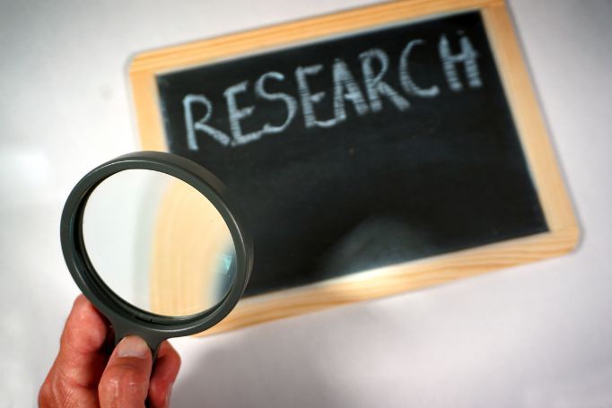 A person is holding a magnifying glass in front of a blackboard that says research