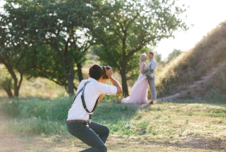 A man is taking a picture of a bride and groom in a field.