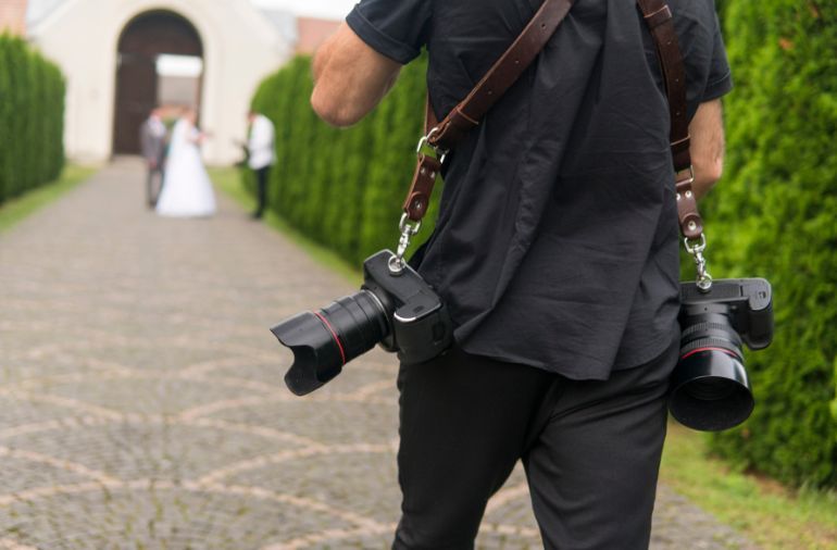 A man is carrying two cameras on his shoulder.