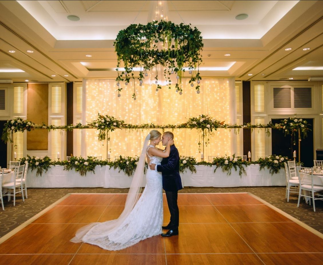 A bride and groom are kissing on a wooden dance floor in a large room.