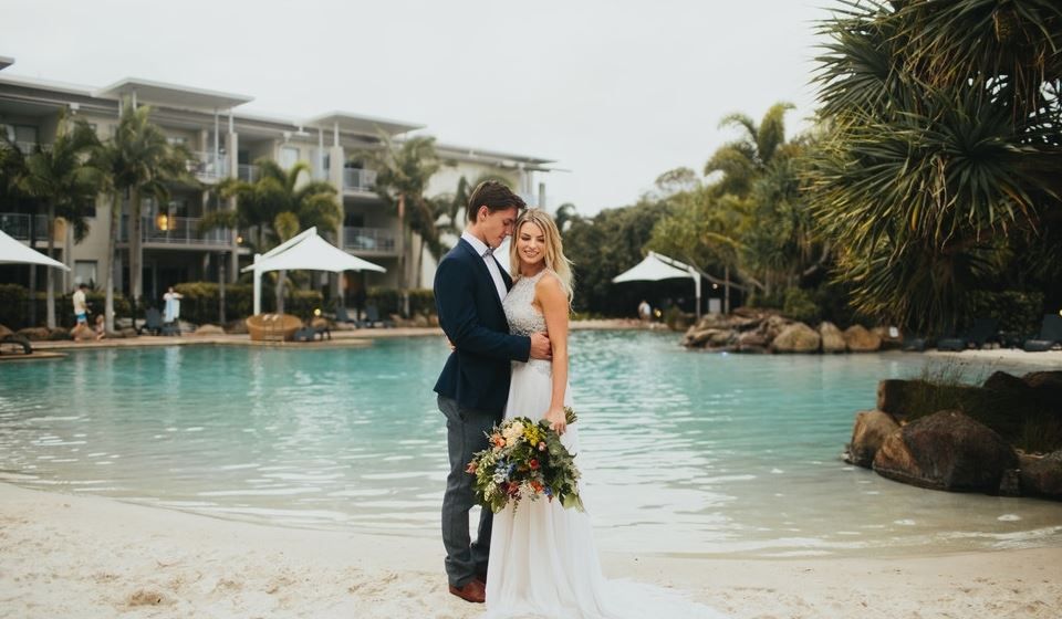 A bride and groom are posing for a picture on the beach.