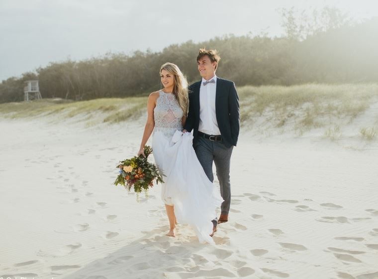 A bride and groom are walking on the beach.