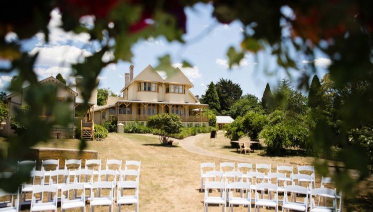 A row of white chairs are lined up in front of a large house.