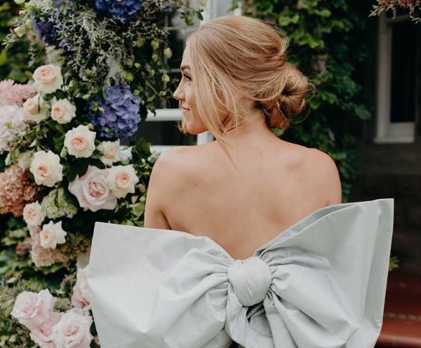 A woman is wearing a white dress with a large bow on the back.