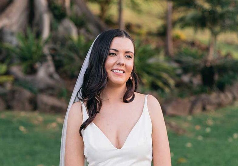 A bride in a white dress and veil is standing in a field.