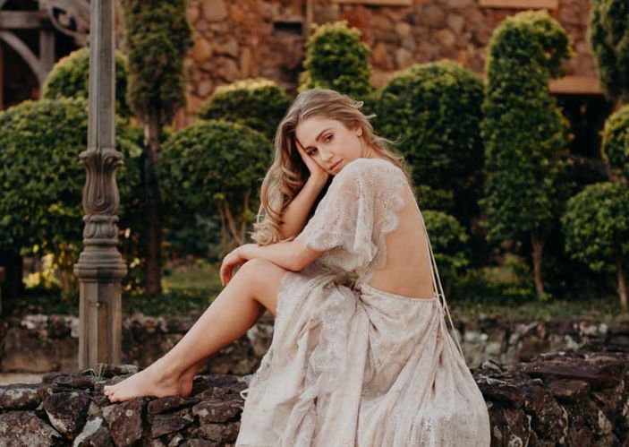 A woman in a white dress is sitting on a stone wall.