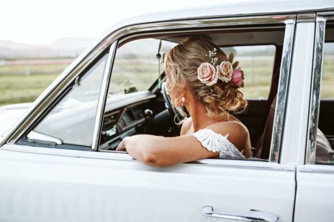 A bride is sitting in a white car looking out the window.