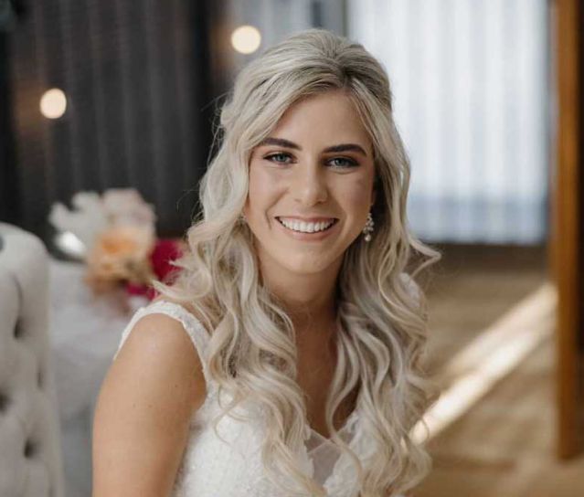 A woman in a white dress is smiling and looking at the camera.