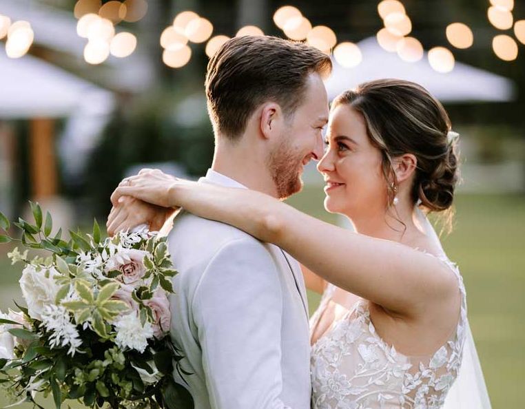 A bride and groom are looking into each other 's eyes while holding a bouquet of flowers.