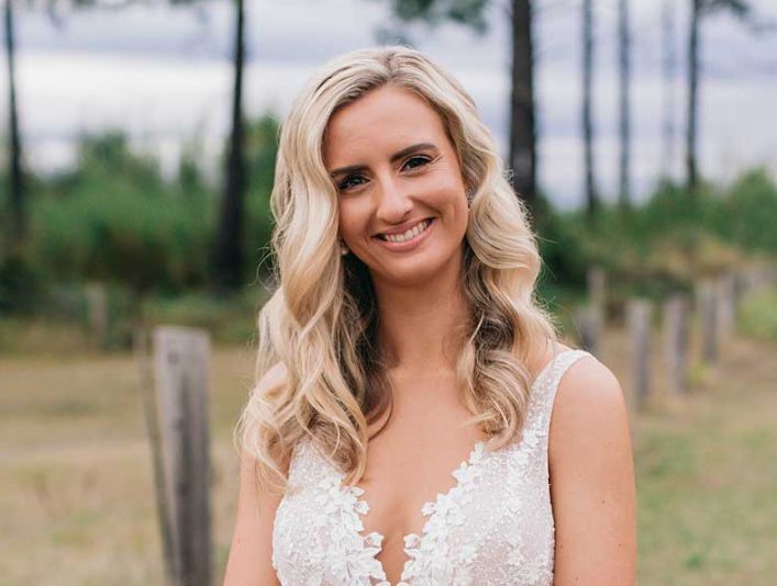 A woman in a wedding dress is standing in a field and smiling.