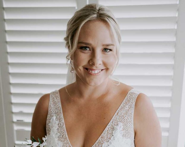 A woman in a wedding dress is smiling in front of a window.