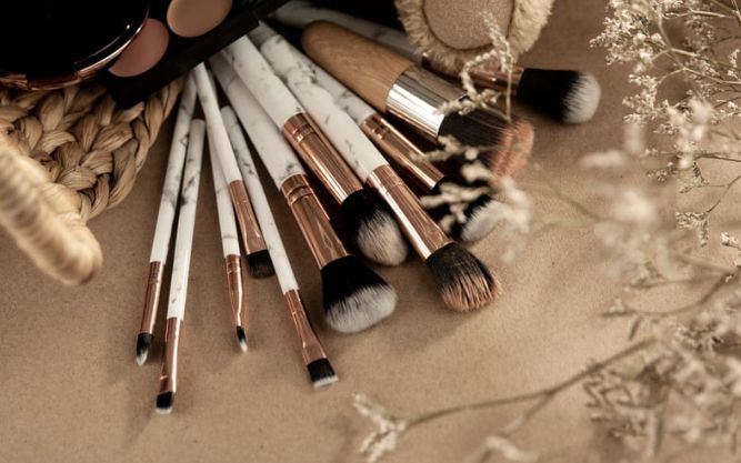 A bunch of makeup brushes are sitting on a table next to a basket of makeup.