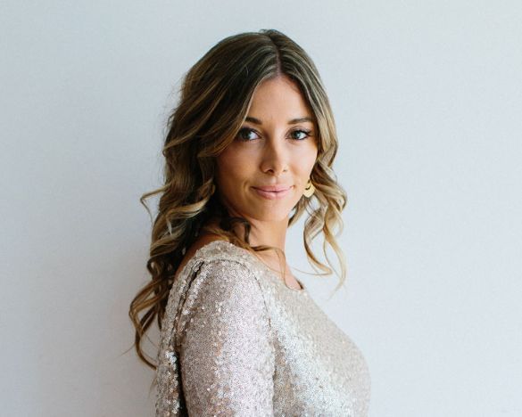 A woman in a sequined dress is standing in front of a white wall.