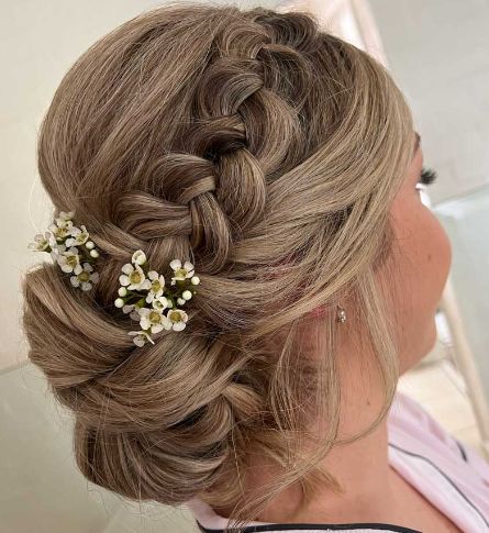 A woman is wearing a braided bun with flowers in her hair.