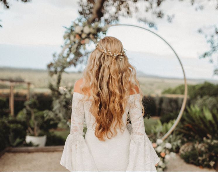 A woman in a wedding dress is standing in front of a floral arch.