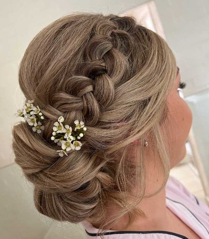 A woman is wearing a braided bun with flowers in her hair.