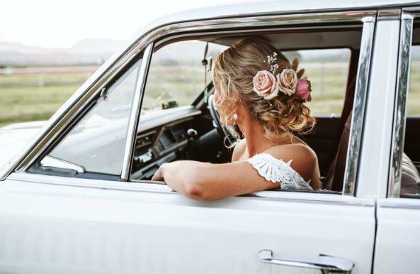 A bride is sitting in a white car looking out the window.