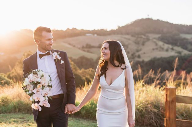 A bride and groom are holding hands and walking in a field.