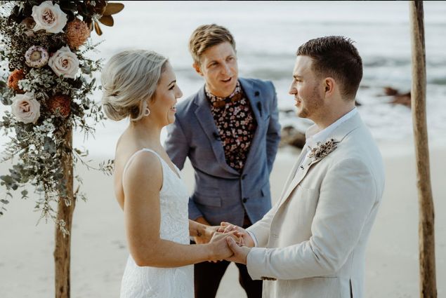 A bride and groom are holding hands during their wedding ceremony on the beach.