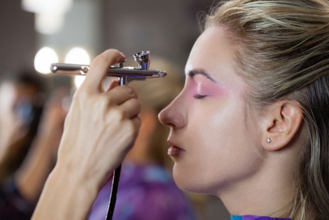 A woman is getting her face painted with an airbrush.