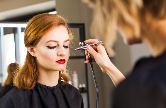 A woman is getting her makeup done by a makeup artist in a salon.