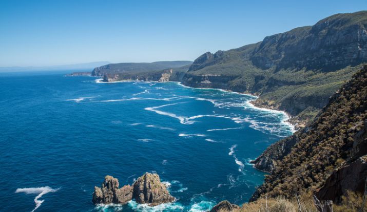 A view of a cliff overlooking the ocean with mountains in the background.