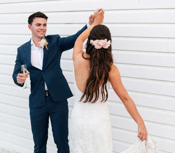 A bride and groom are dancing in front of a white wall.