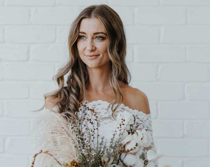 A woman in a white off the shoulder dress is holding a bouquet of flowers.