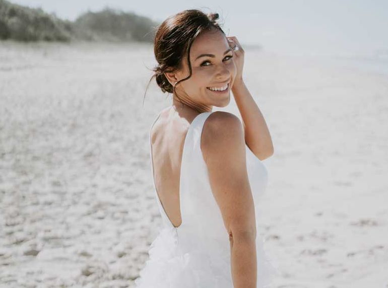 A woman in a white dress is standing on a beach.