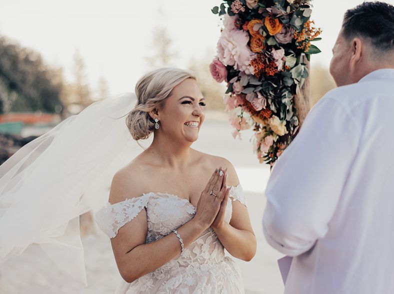 A bride and groom are holding hands during their wedding ceremony on the beach.