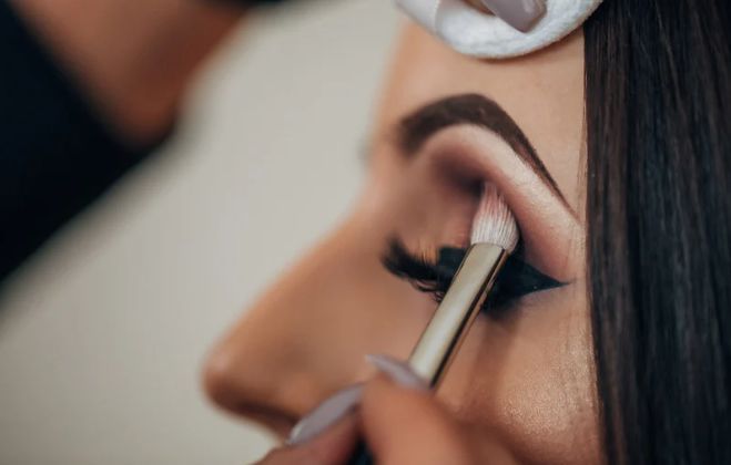 A woman is getting her eye makeup done by a makeup artist.