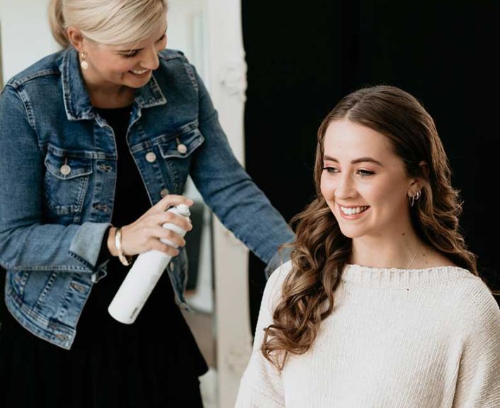 A woman is spraying hairspray on another woman 's hair.