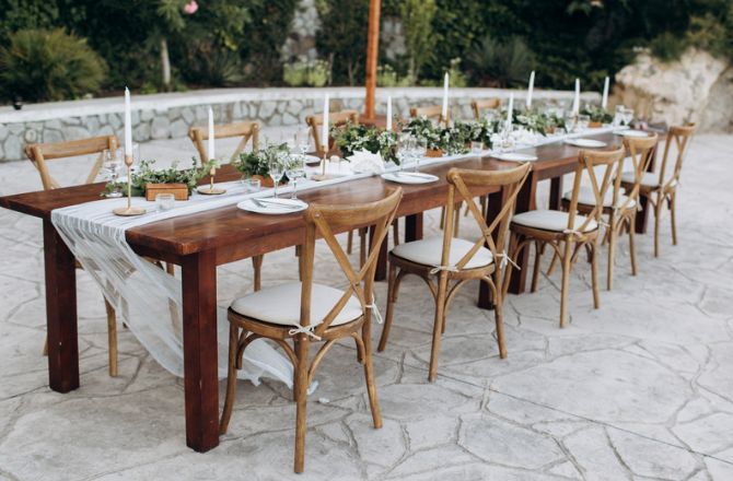 A long wooden table and chairs are set for a wedding reception.