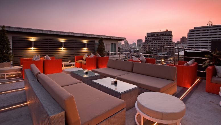 A rooftop patio with a lot of furniture and a sunset in the background