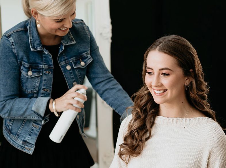 A woman is spraying hairspray on another woman 's hair.