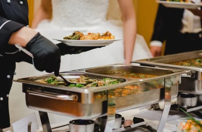 A chef is serving food to a bride and groom at a wedding reception.