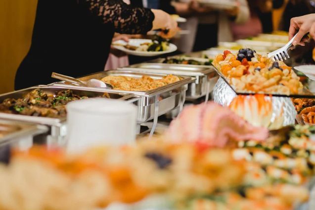 A woman is taking a plate of food from a buffet table.