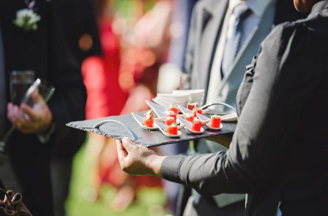 A woman is holding a tray of food in front of a group of people.