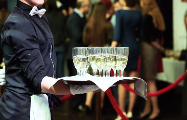 A waiter is holding a tray of champagne glasses at a party.