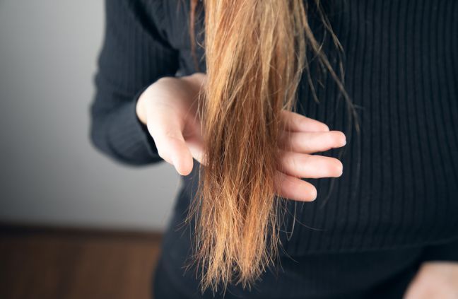 A woman is holding her hair in her hands and looking at it.