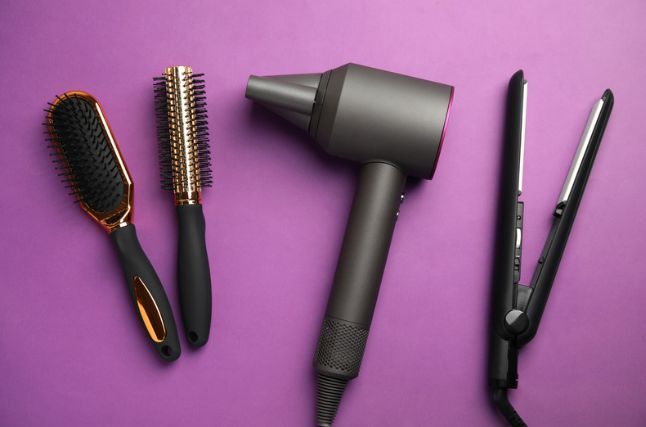 A hair dryer , brush , and straightener on a purple background.