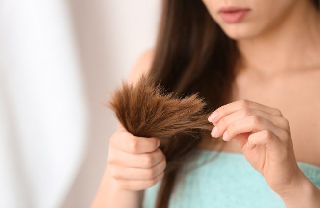 A woman is holding a piece of her hair in her hands.