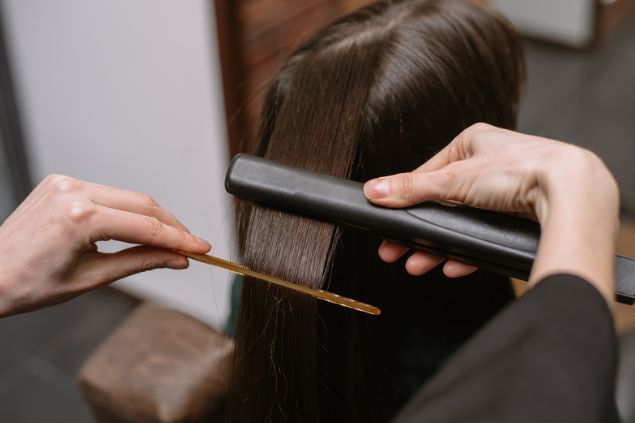 A woman is getting her hair straightened by a hairdresser.