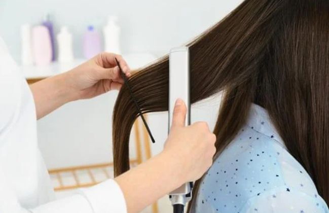 A woman is getting her hair straightened by a hairdresser.