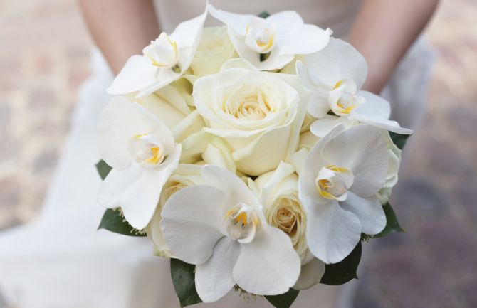 A bride is holding a bouquet of white roses and orchids.