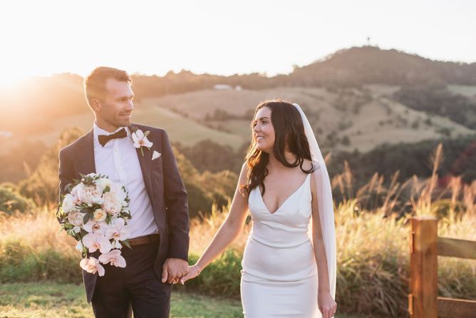 A bride and groom are holding hands while walking in a field.