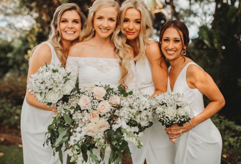 A bride and her bridesmaids are posing for a picture while holding bouquets of flowers.