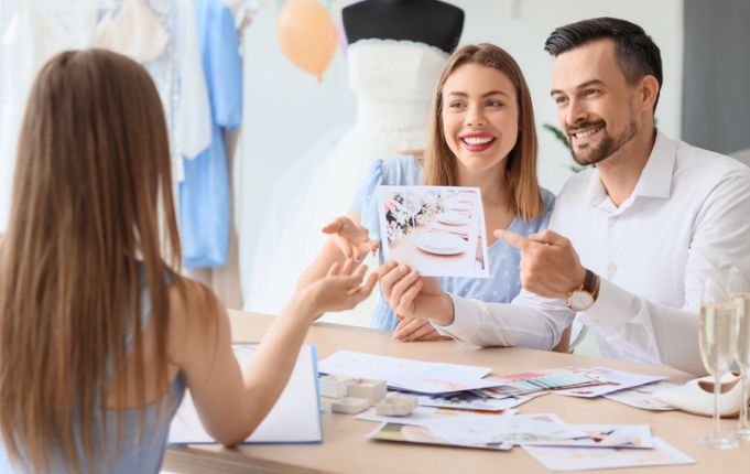 A man and a woman are sitting at a table looking at a wedding dress.