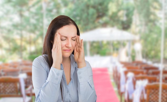 A woman is holding her head in pain in front of a wedding.