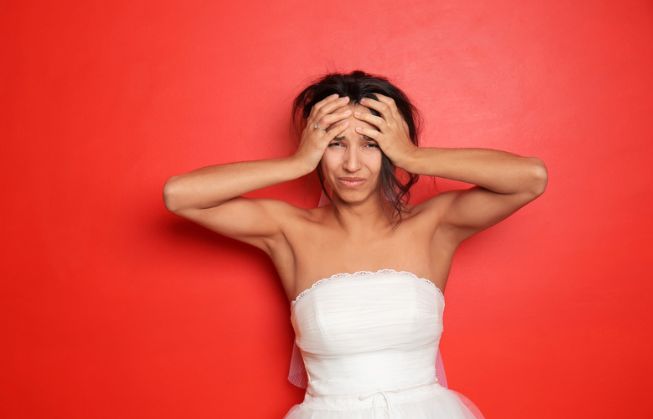 A woman in a wedding dress is holding her head in her hands.